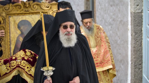 A priest in a black robe carries a candle next to an icon during a religious procession, Orthodox