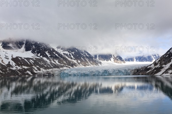 An impressive lake reflects the surrounding glaciers and mountains, surrounded by clouds and a calm