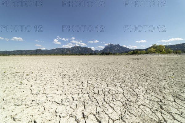 Cracked, dried out ground, waterless Forggensee in spring, behind it Tegelberg massif and Säuling,