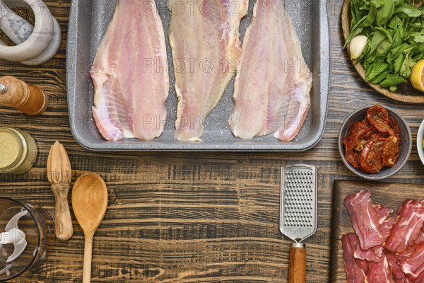 Fresh fish fillets are laid out on a baking tray, surrounded by various ingredients including