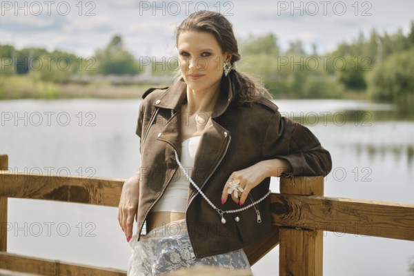 A model stands confidently near a tranquil water body, showcasing a fashionable outfit complete