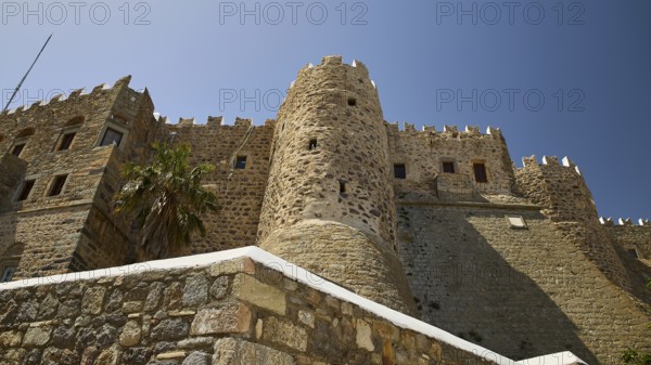 Medieval stone castle with palm trees and blue sky, imposing architecture, Monastery of St John the