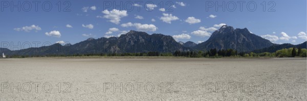 Cracked, dried out ground, waterless Forggensee in spring, behind it Tegelberg massif and Säuling,