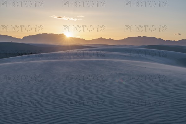 Rays of light over the mountains highlight windblown sand at sunset at White Sands National Park in