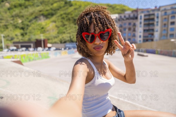 Fashionable young woman with heart shaped sunglasses making peace sign while taking a selfie in