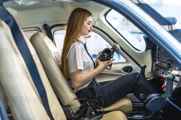 Young woman pilot checking her headset while sitting in the cockpit of a small aircraft, preparing