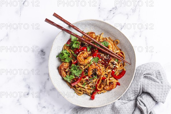 Udon noodles, shrimp with vegetables and fresh herbs, in a bowl with chopsticks, light background,