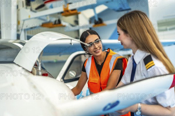 Female pilot and aircraft maintenance technician working together in hangar, discussing maintenance