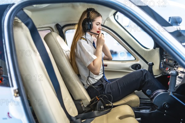 Female pilot sitting in the cockpit of a small aircraft, wearing a headset and communicating,