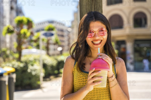 Smiling woman with pink sunglasses enjoying a refreshing fruit smoothie on a sunny summer day in