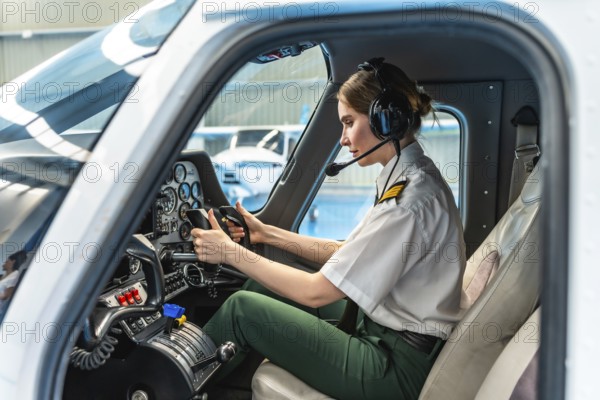 Confident female pilot wearing headset and holding steering wheel while sitting in cockpit of