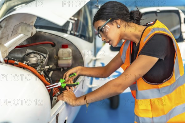Young woman aircraft mechanic wearing safety glasses and high visibility vest using pliers while
