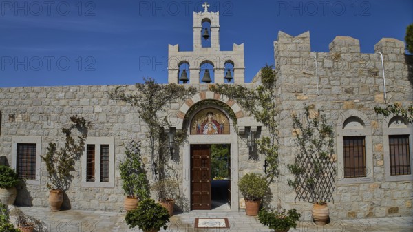 Church façade with bell tower and religious icon, surrounded by plants, woman's monastery,