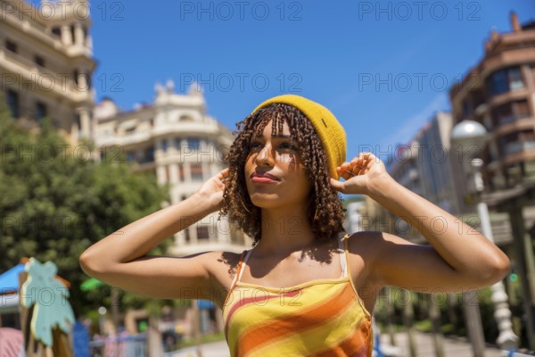 Young woman adjusting her yellow beanie in valencia city center, enjoying a sunny summer day