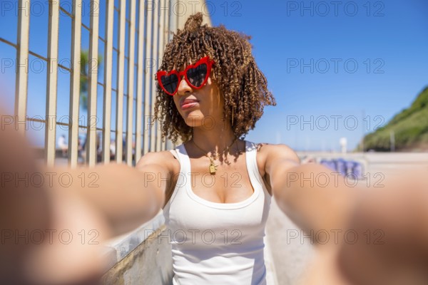 Portrait of a young woman with curly hair taking a selfie wearing heart shaped sunglasses by the