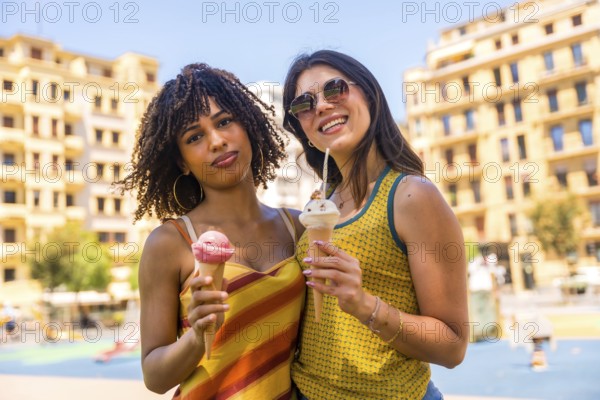 Two female friends enjoying ice cream cones together on a sunny summer day in a city park, sharing