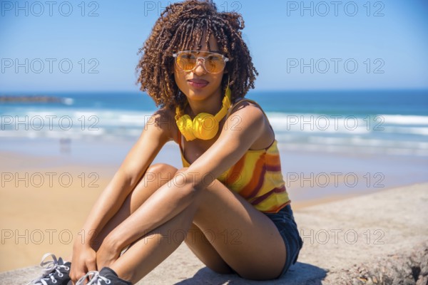 Fashionable young woman enjoying the summer sun and music on a beach wall, embracing the carefree