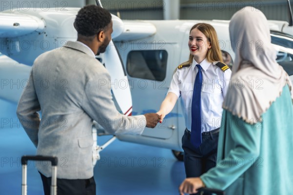 Female pilot shaking hands with businessman next to a private airplane inside an hangar, a