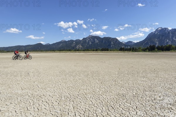 Cracked, dried out ground, waterless Forggensee in spring, behind it Tegelberg massif and Säuling,