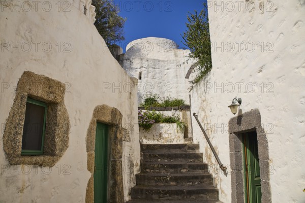 Whitewashed buildings with stone details and green doors under a clear blue sky, Monastery of the
