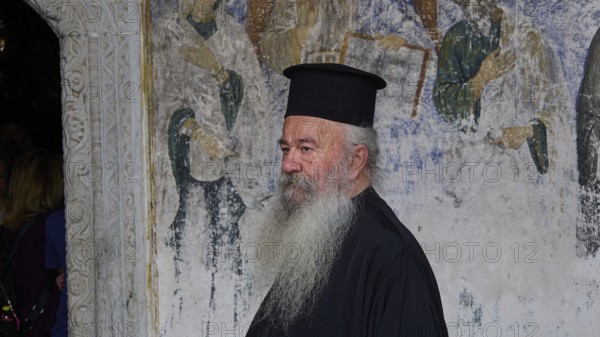 Priest in clerical garb in front of a religious mural, Monastery of St John the Theologian,