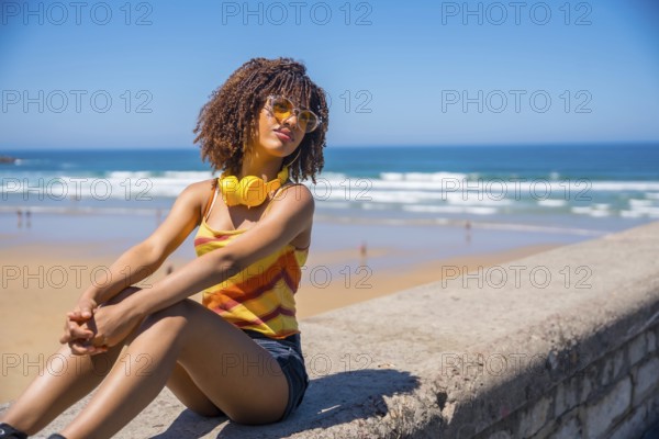 Young woman soaking up the summer sun and ocean breeze, enjoying music through her headphones while