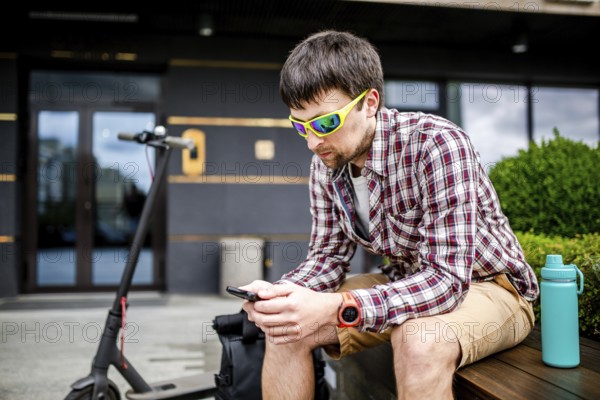 Individual urban environmental friendly transport electric kick scooter parked near man sitting on