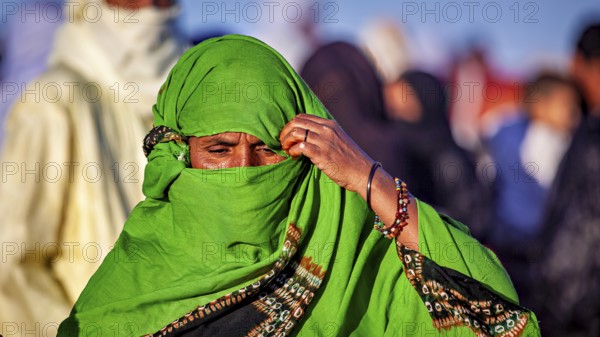 A woman in a green robe and jewellery pensively covers her face, Veiled woman at the Tamanrasett