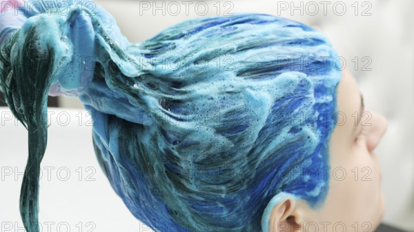 Professional hairdresser holds client's long blue hair in hand while washing hair after process of
