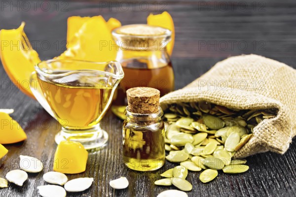 Pumpkin oil in vial, gravy boat and a jar, seeds in a bag and on table, slices of vegetable on