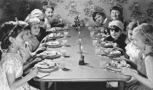 Children in the 1950s. Girls and boys dressed up in hats and costumes are sitting a table together