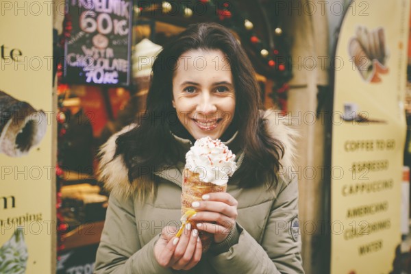 A beautiful girl in a warm jacket eats trdelnik or Trdlo with cream in her hands, in the winter in