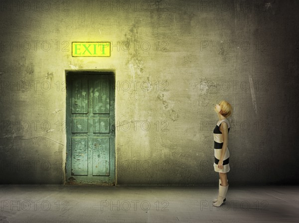Young woman in black and white dress stand in front of blue door in dark grungy room watch on