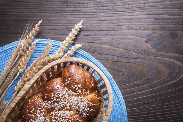 Sweet roll in wicker basket wheat rye ears with wattled table-cloth on wooden vintage board food