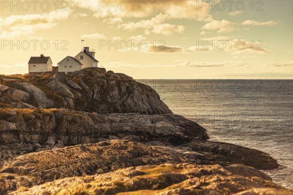 A lighthouse and house on rocky cliffs by the ocean at sunset, creating a serene coastal scene,