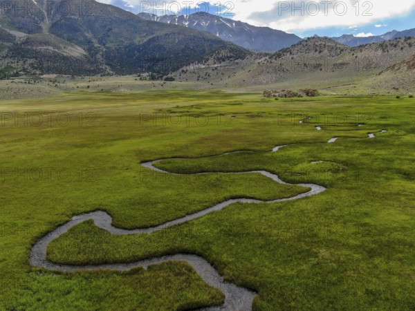 Aerial view of green land and small curve river with mountain in the background in Aspen Springs,