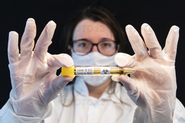 Selective focus shot of vial filled with urine sample and labeled Covid-19 test, held center frame