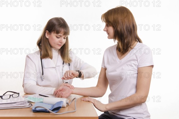 Physician at the table checks the pulse of a patient