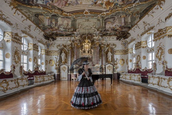 A woman in a black dress stands in a magnificent room with frescoed ceilings, staged photo shoot,