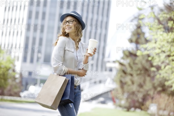 Happy young trendy woman drinking a takeaway coffee and walking with shopping bags after shopping