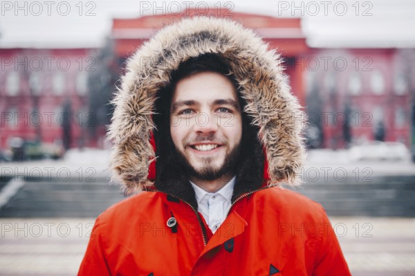 Portrait, close-up of young stylishly man smiling with a beard dressed in red winter jacket with a