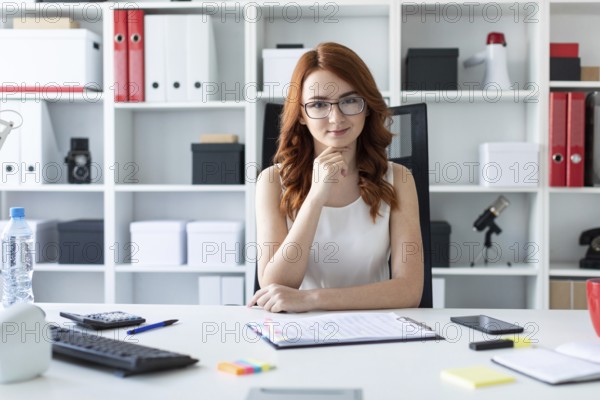 A red-haired young girl with glasses, a white blouse and a red skirt is working in the office.