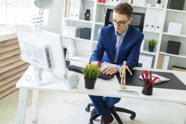 A handsome young man with glasses, a blue suit and a light shirt is working in the office. photo