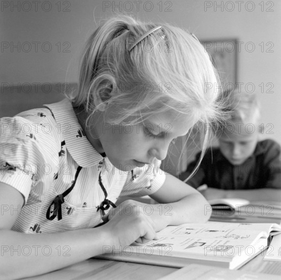 School in the 1950s. A girl is seen sitting at her desk in the classroom reading from the