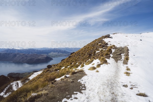 A mountain path with snow offers an impressive view of a lake and mountains, Roys Peak, Wanaka, New