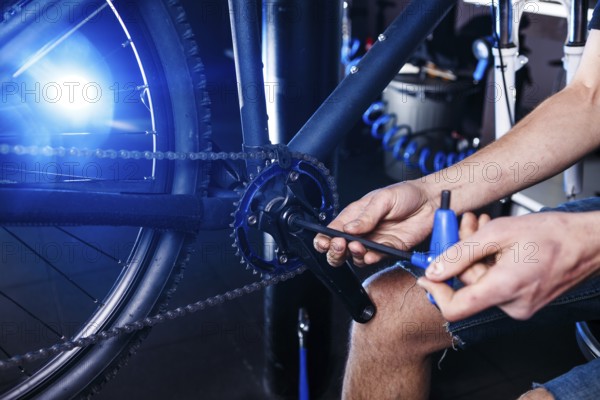A close-up of a male bicycle mechanic's hand in the workshop uses a screwdriver tool to adjust and