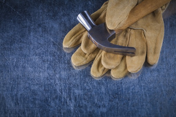 Pair of leather protective gloves with metal claw hammer on scratched metallic background