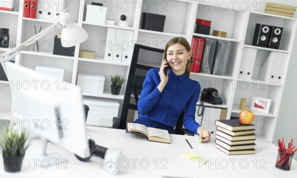 A young girl is sitting at a computer desk, holding a yellow marker in her hand and talking on the