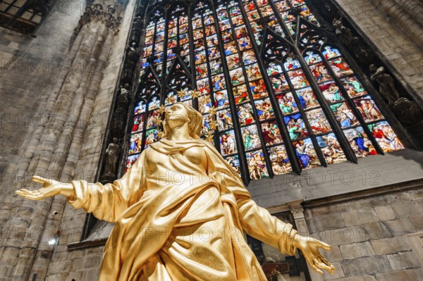 Statue of Madonna in gold against the background of a stained glass window in the Duomo. Milan,