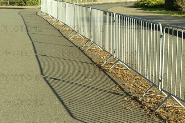 Metal crowd control barriers casting long shadows on an asphalt road